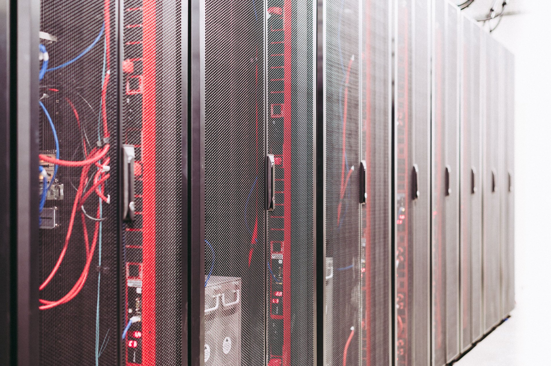 Filas de racks de servidores en centro de datos oscuro con cables rojos y azules visibles, perspectiva con profundidad