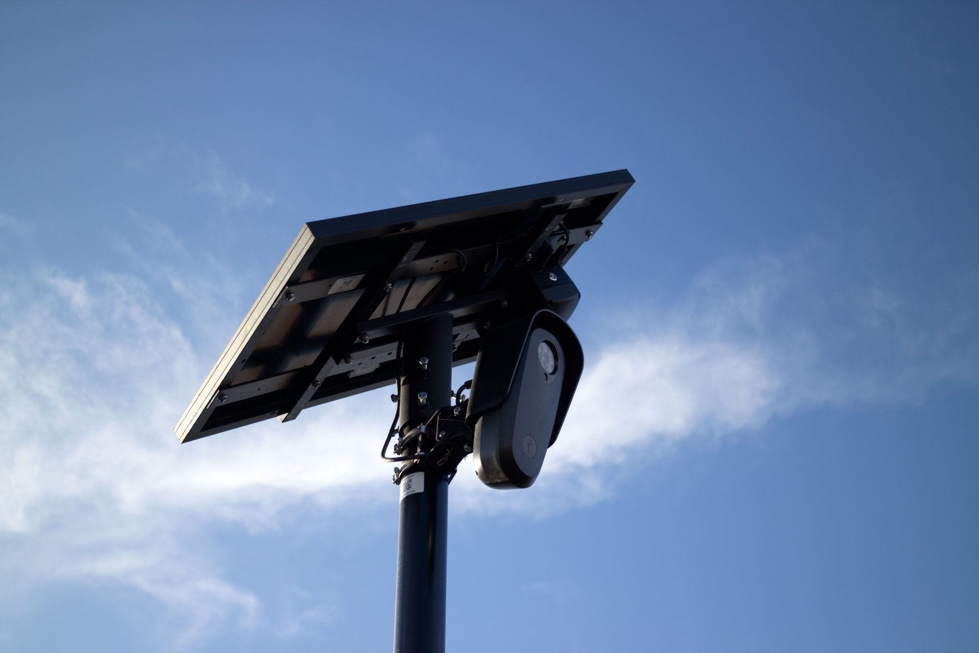 Cámara de vigilancia con panel solar montada en un poste urbano contra el cielo azul