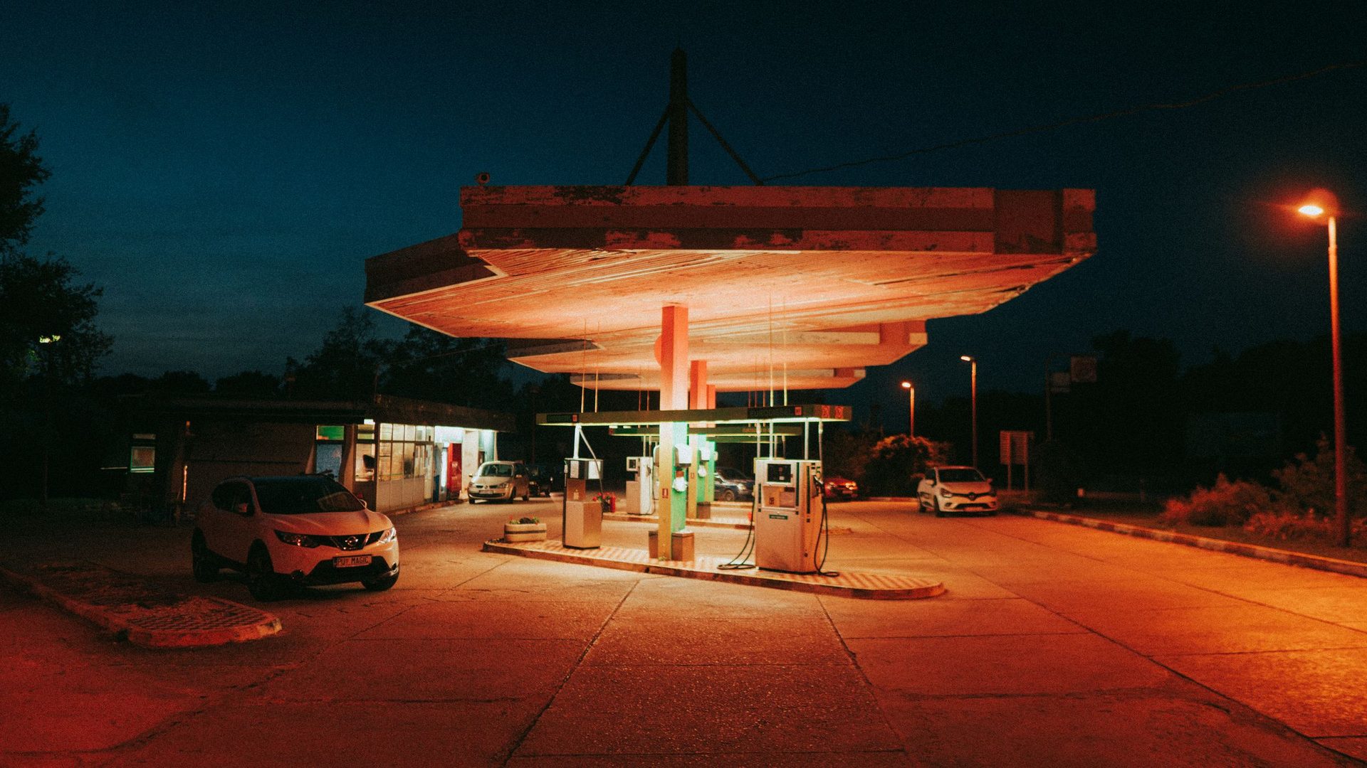 Estación de servicio iluminada de noche con dos islas de bombas y un vehículo saliendo del forecourt