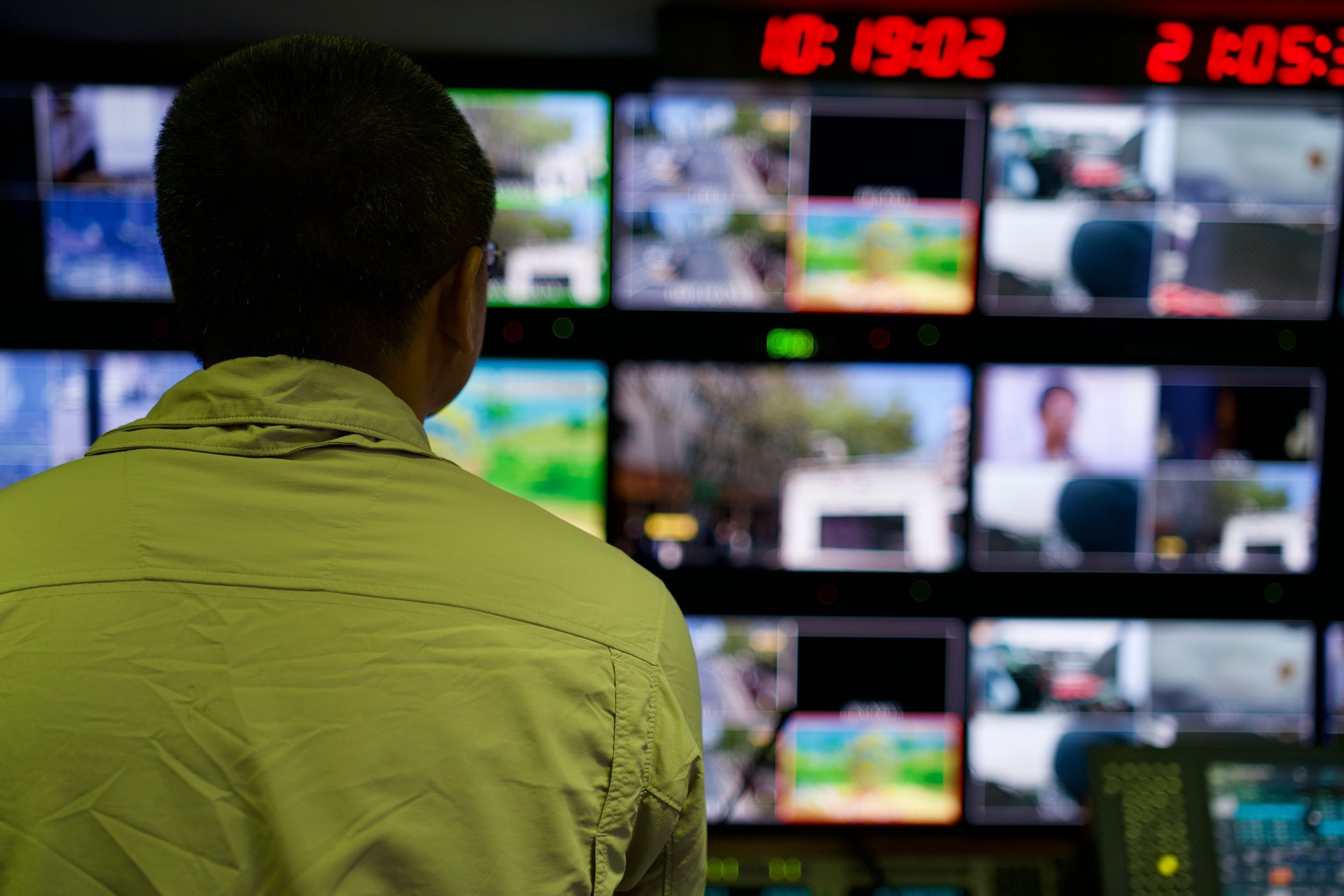 Operador en sala de control revisando múltiples pantallas CCTV en pared de video oscura, ambiente de fatiga operativa