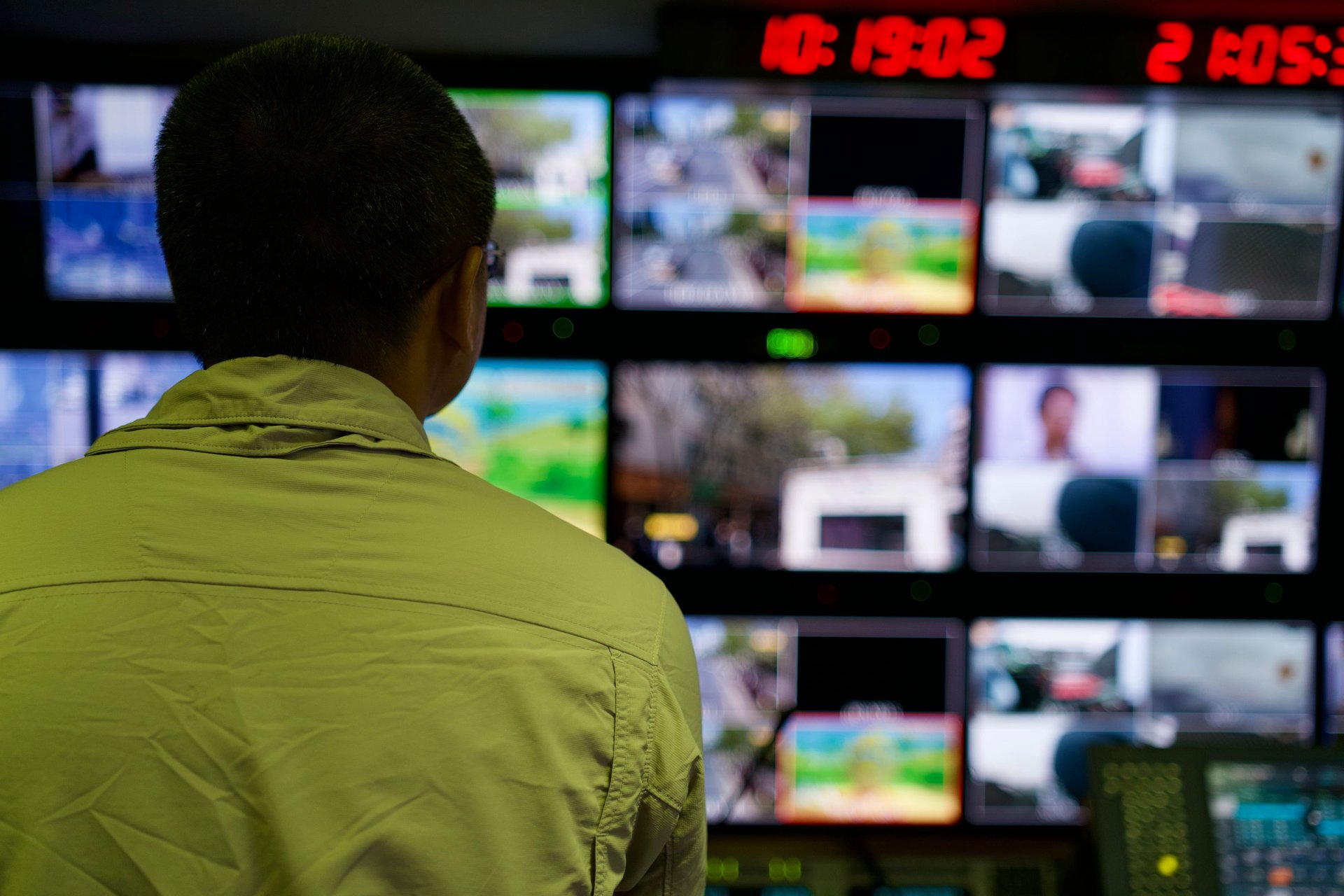 Operador de CCTV en sala oscura monitoreando matriz de más de 16 monitores, ambiente de fatiga atencional