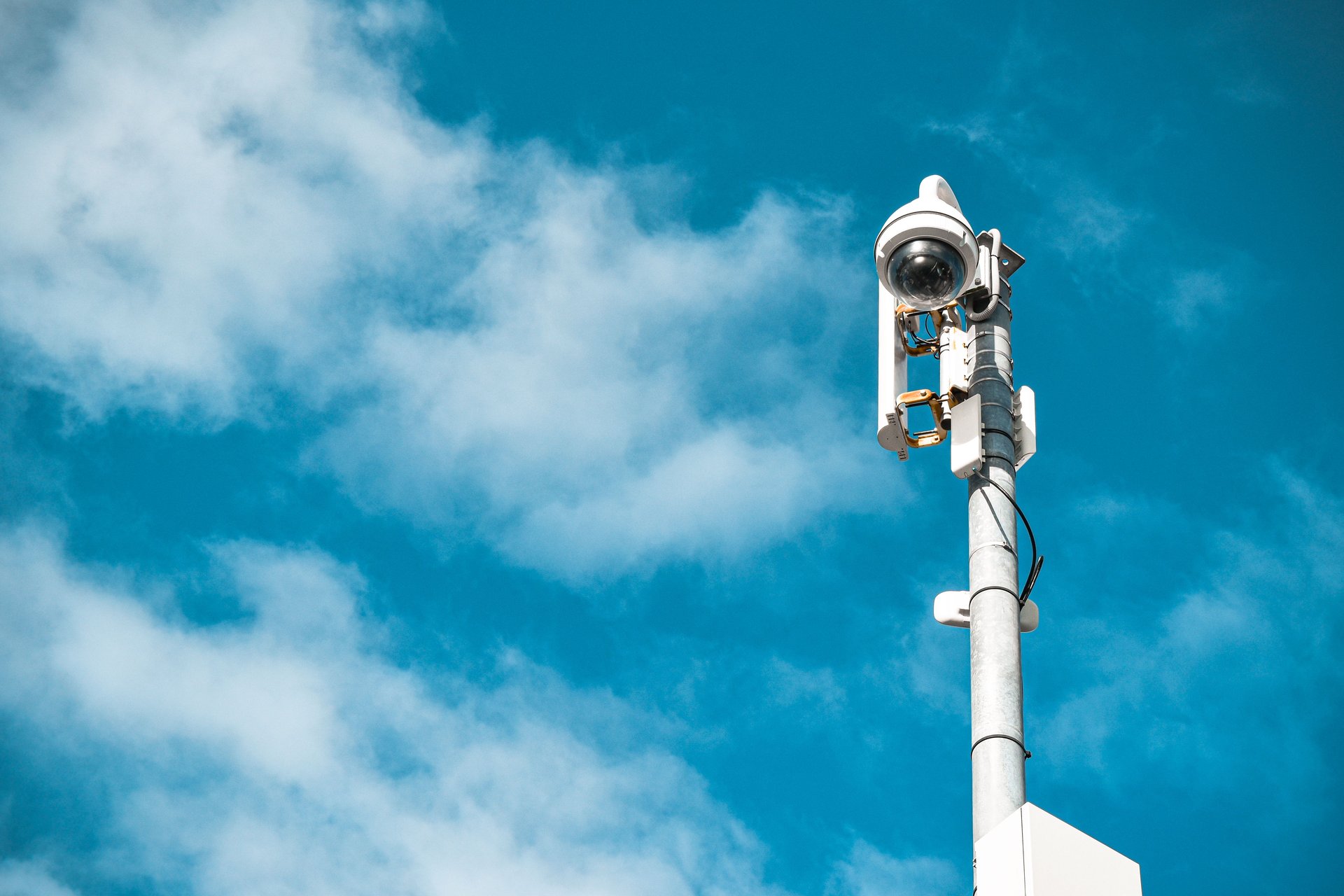 Cámara de seguridad urbana montada en poste con cables visibles y placa metálica — infraestructura de vigilancia en espacio público