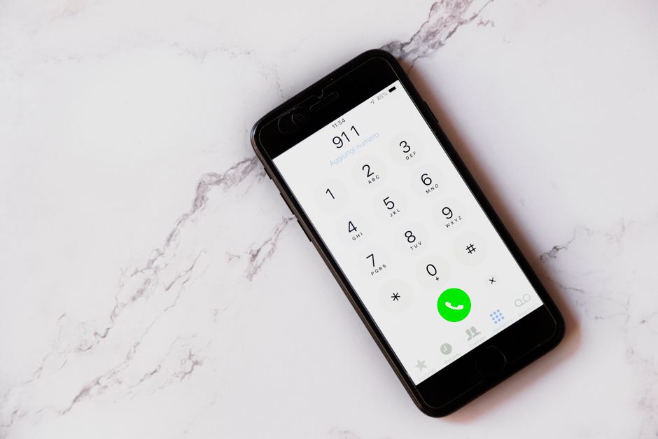 Smartphone sobre superficie mármol mostrando el teclado con 911 marcado, metáfora de la llamada que un técnico de Flock Safety hizo contra un reportero que filmaba una cámara en público
