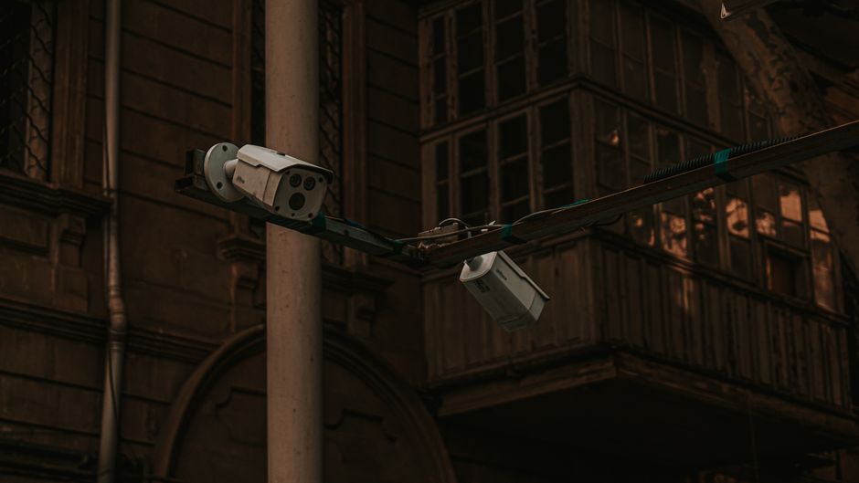 Postes urbanos de CCTV con cableado visible — infraestructura de vigilancia masiva en arquitectura pública
