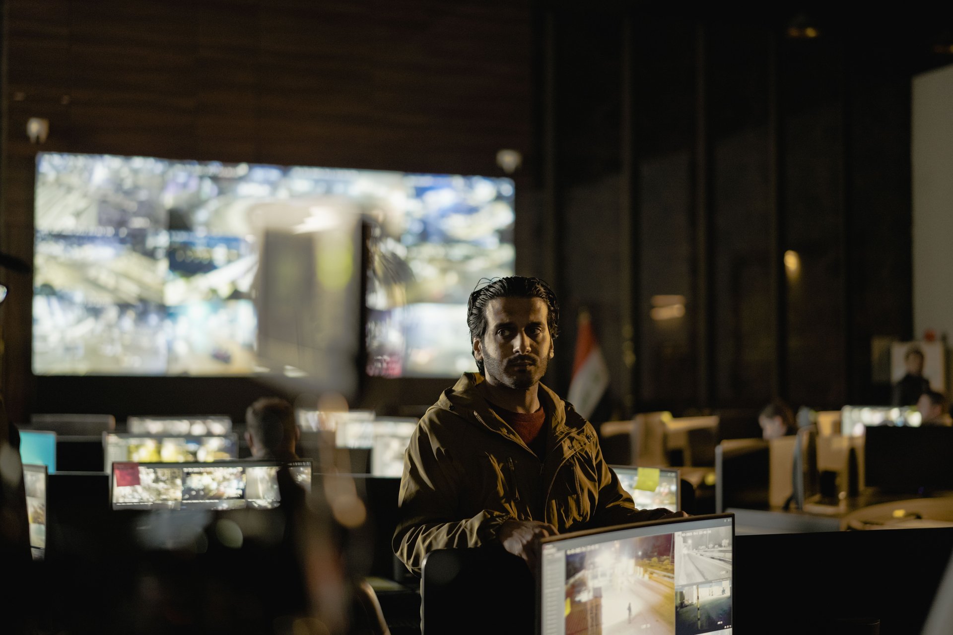 Operador en sala de control con video wall de múltiples monitores mostrando footage de cámaras — un vendor moderando búsquedas contra cámaras de clientes