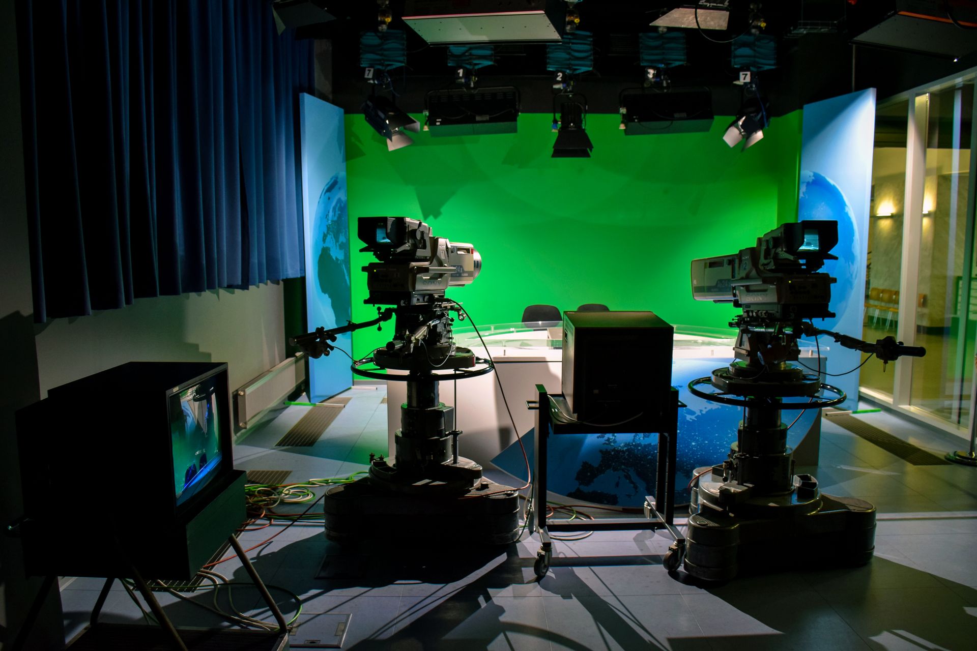 Estudio de TV con chroma key verde y tres cámaras broadcast profesionales apuntando al set, ilustrando cómo se coordina un paquete noticiero