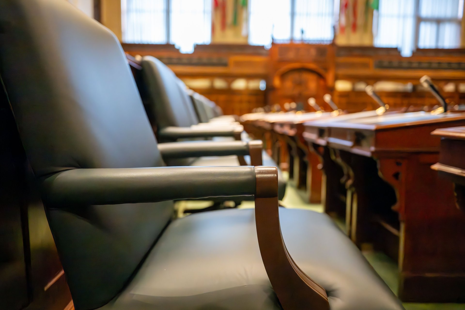 Sala de audiencia legislativa vacía con sillas de cuero y escritorios de madera con micrófonos — la arquitectura institucional del Senado donde los CEOs de Flock, Axon, Motorola y Verkada testificarán el 23 de septiembre