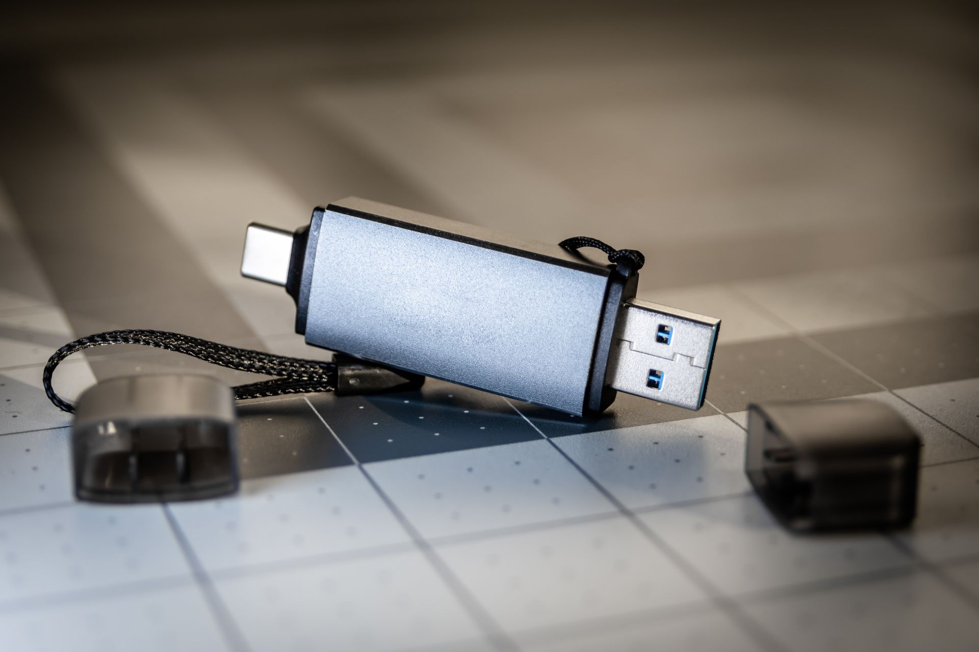 Close-up editorial de un conector USB-C oscuro sobre superficie gris cuadriculada — dispositivo de vigilancia clandestina