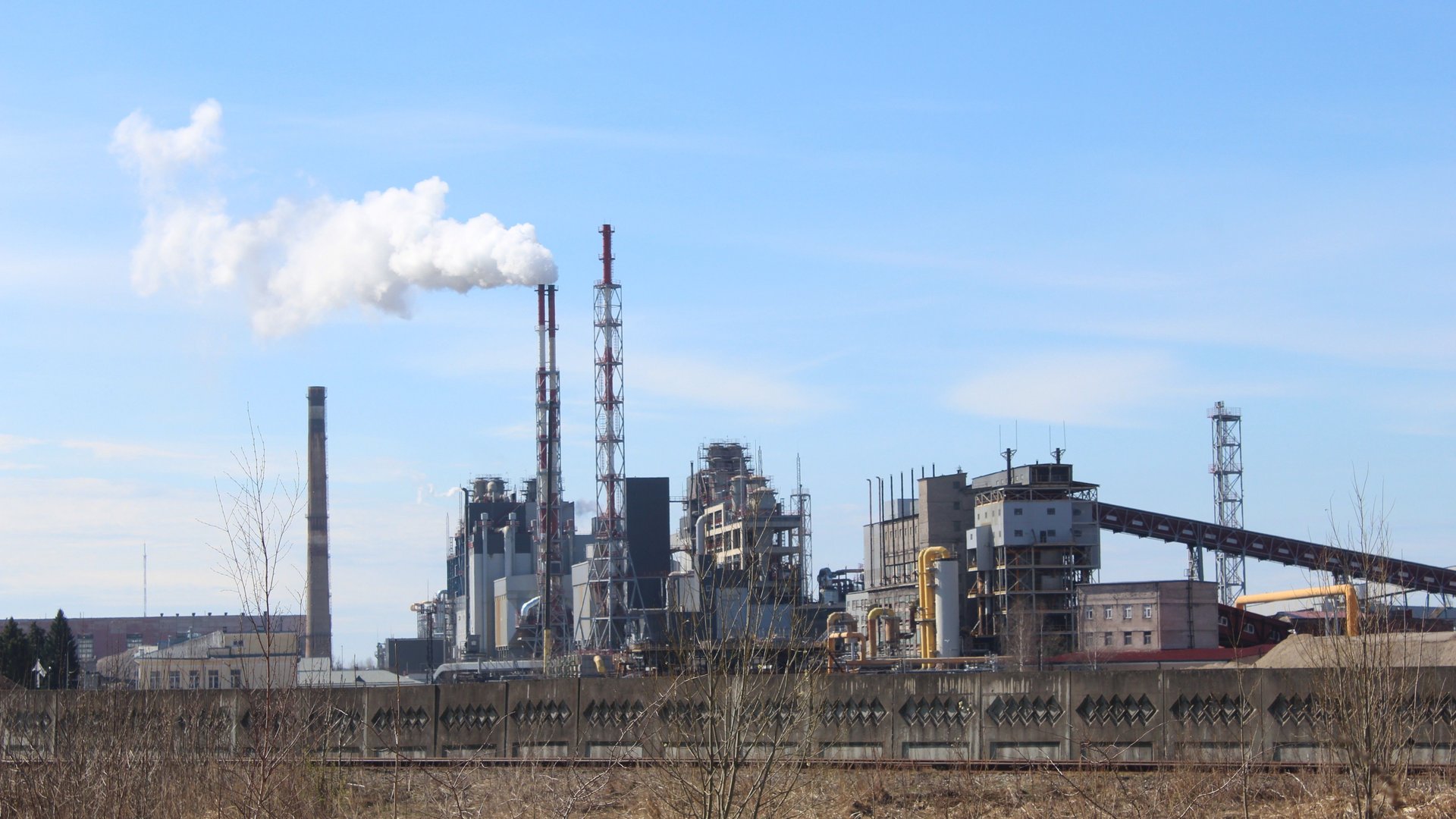 Planta industrial con chimeneas emitiendo humo bajo el cielo azul despejado